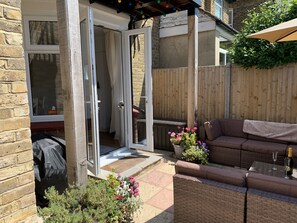 A patio area with a wicker sofa, a table with glasses, and a potted plant with flowers.