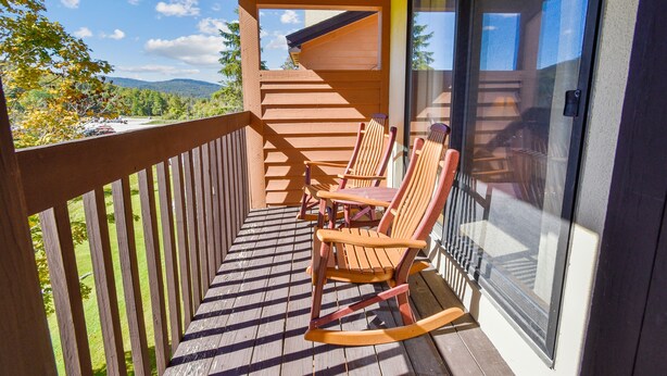 Eine Holzterrasse mit Schaukelstühlen und einem Tisch, mit Blick auf eine malerische Landschaft aus Bäumen und Bergen.