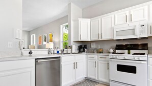 Una cocina moderna con armarios blancos, lavavajillas de acero inoxidable, microondas y estufa.