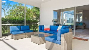 Un espacio exterior moderno con mobiliario de mimbre y una mesa de centro de cristal.