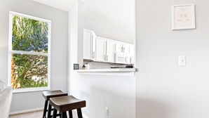 Una cocina con armarios blancos, microondas y ventana con vista a árboles.