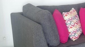 Un sofá gris con dos almohadas rosas y una multicolor frente a una pared blanca.