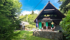 A rustic wooden cabin with a stone foundation, surrounded by lush greenery and trees.