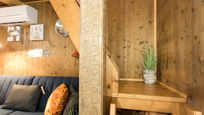 A wooden interior with a sofa, cushions, a clock, and a potted plant.