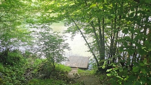 A stone pathway leading to a wooden dock by a lake, surrounded by lush greenery.