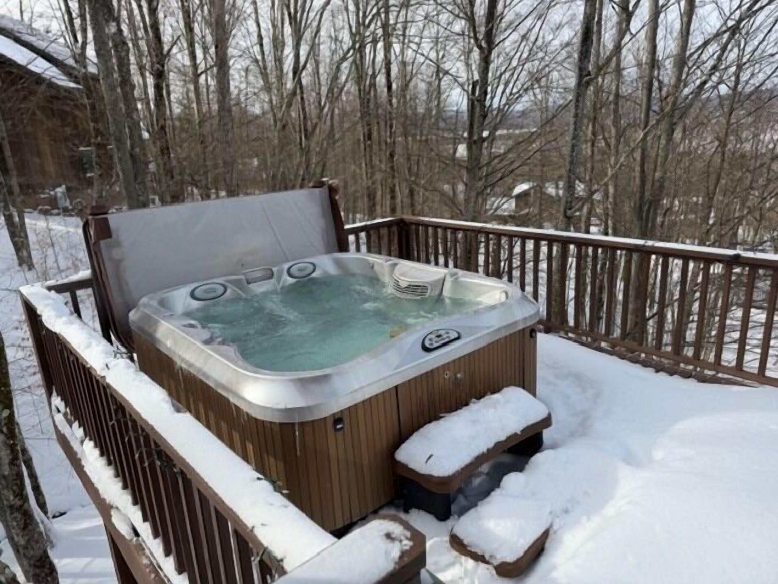 A hot tub on a wooden deck surrounded by snow.