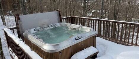 A hot tub on a wooden deck surrounded by snow.