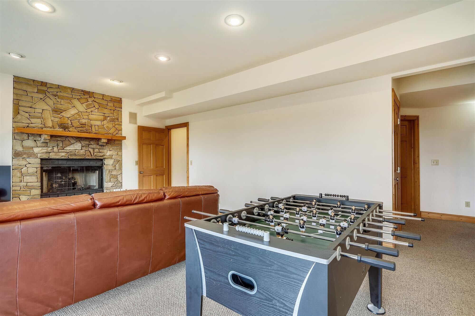 A room with a foosball table, a stone fireplace, and a leather couch.