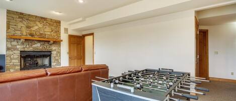 A room with a foosball table, a stone fireplace, and a leather couch.
