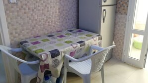 Een compacte keuken met een betegelde achterwand, een koelkast, een tafel met een kleurrijke tafelkleed en twee stoelen.