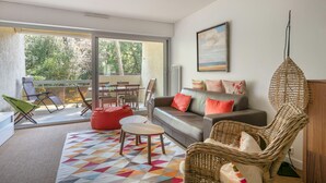 Ein Wohnzimmer mit einer Couch, Stühlen, einem Tisch und einem Balkon mit Blick auf Bäume.