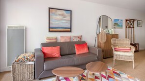 Ein Wohnzimmer mit einem grauen Sofa, zwei Holztischen, einem Korbwannenaufsatz und einem farbenfrohen Teppich.