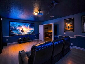 A home theater room with a large flat-screen TV, a reclining leather couch, and a projector mounted on the ceiling. - Private Movie Theater! Up to 20 Guests! (Davenport)
