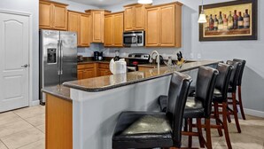 A modern kitchen with wooden cabinets, stainless steel appliances, a granite countertop, and a bar area with leather chairs. - Private Movie Theater!  Up to 20 Guests! (Davenport)