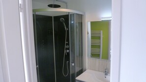A modern bathroom with a glass-enclosed shower, a white sink, and a green wall. - Le 232 - Logements (Chasseneuil-du-Poitou)