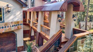 Un edificio de varios niveles con una escalera de madera, un espacio al aire libre cubierto y vistas del bosque circundante.