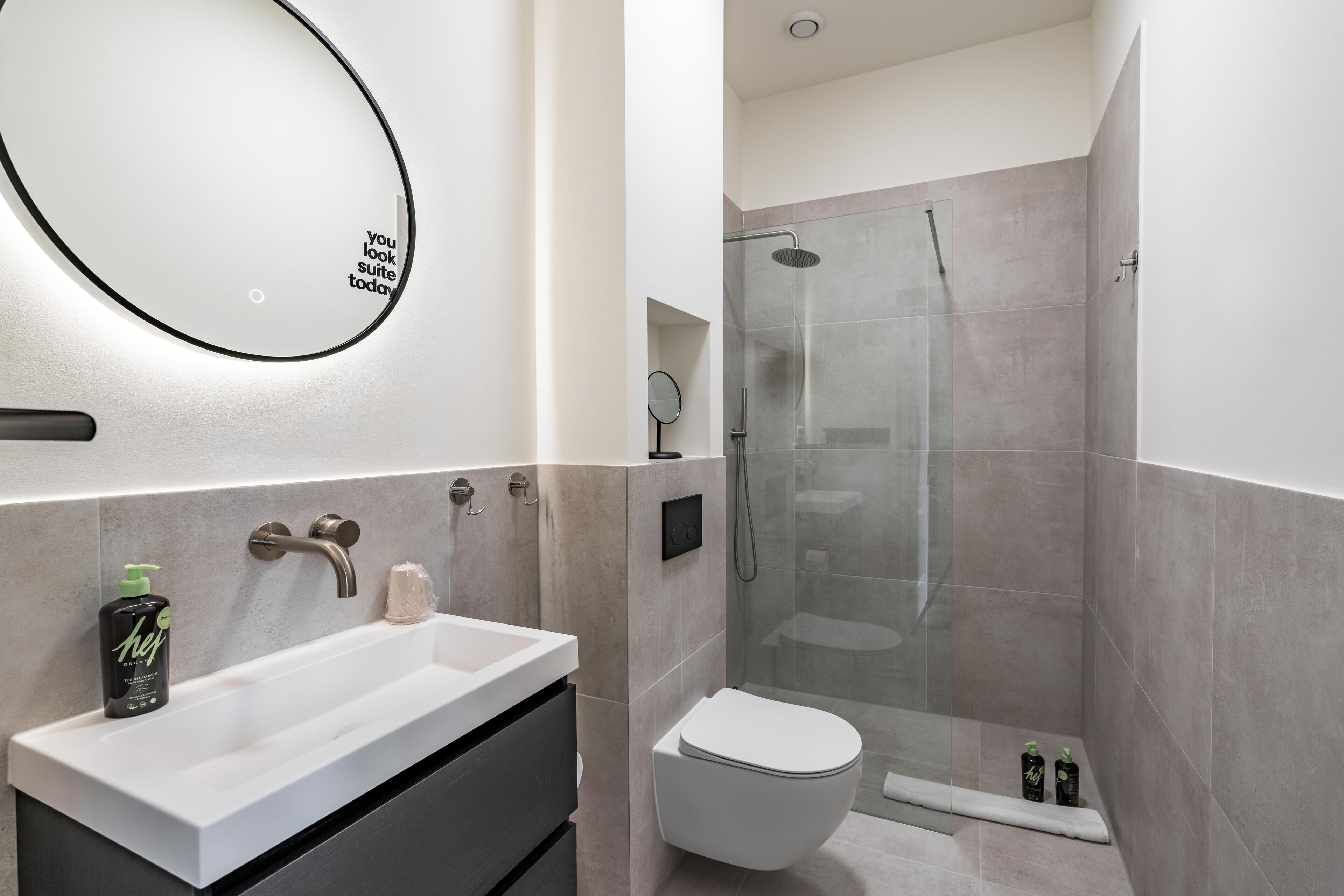 A modern bathroom with a white sink, a round mirror, a toilet, and a glass-enclosed shower area.