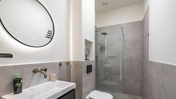 A modern bathroom with a white sink, a round mirror, a toilet, and a glass-enclosed shower area.