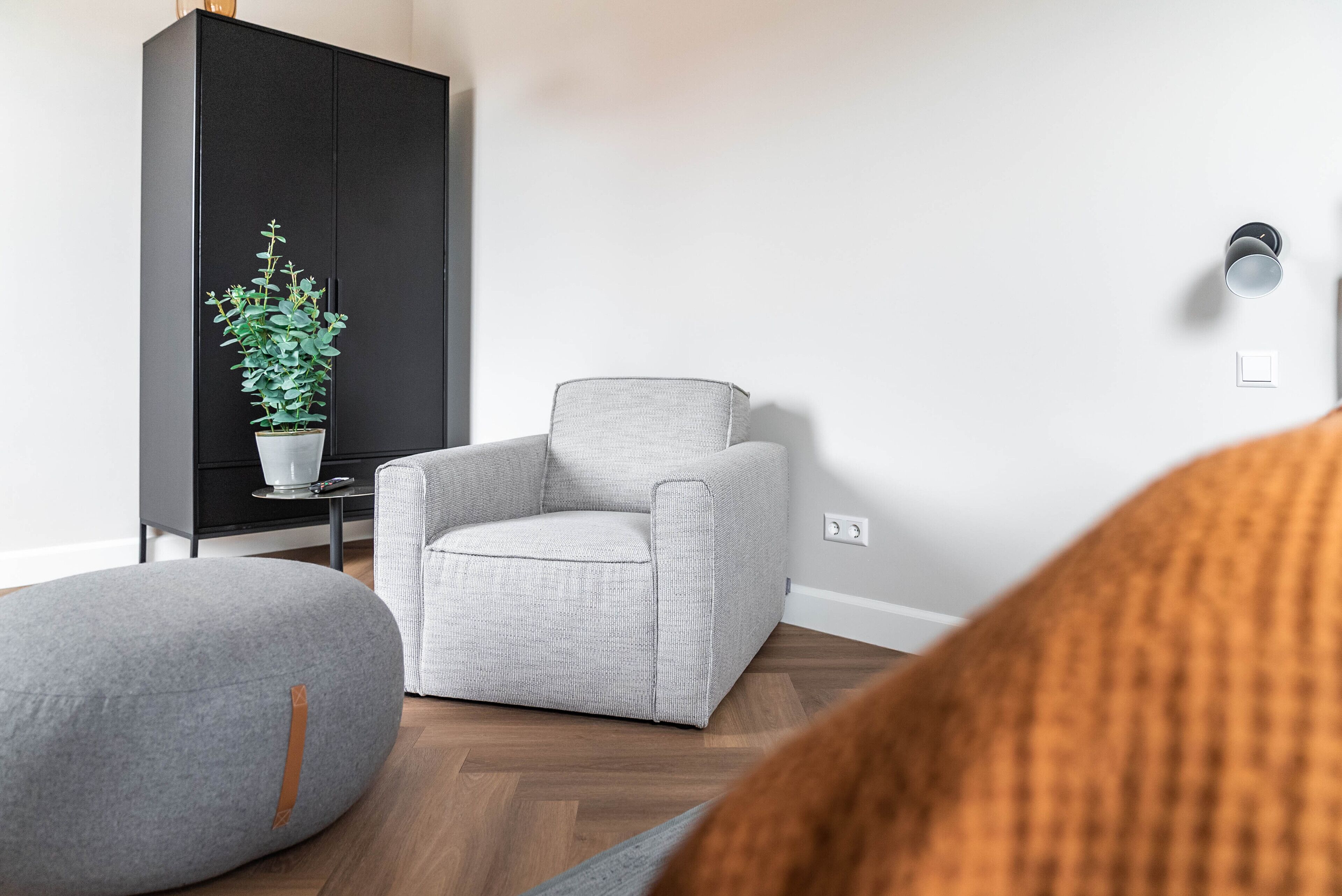 Un salon moderne avec un fauteuil gris, un pouf gris et une plante en pot.