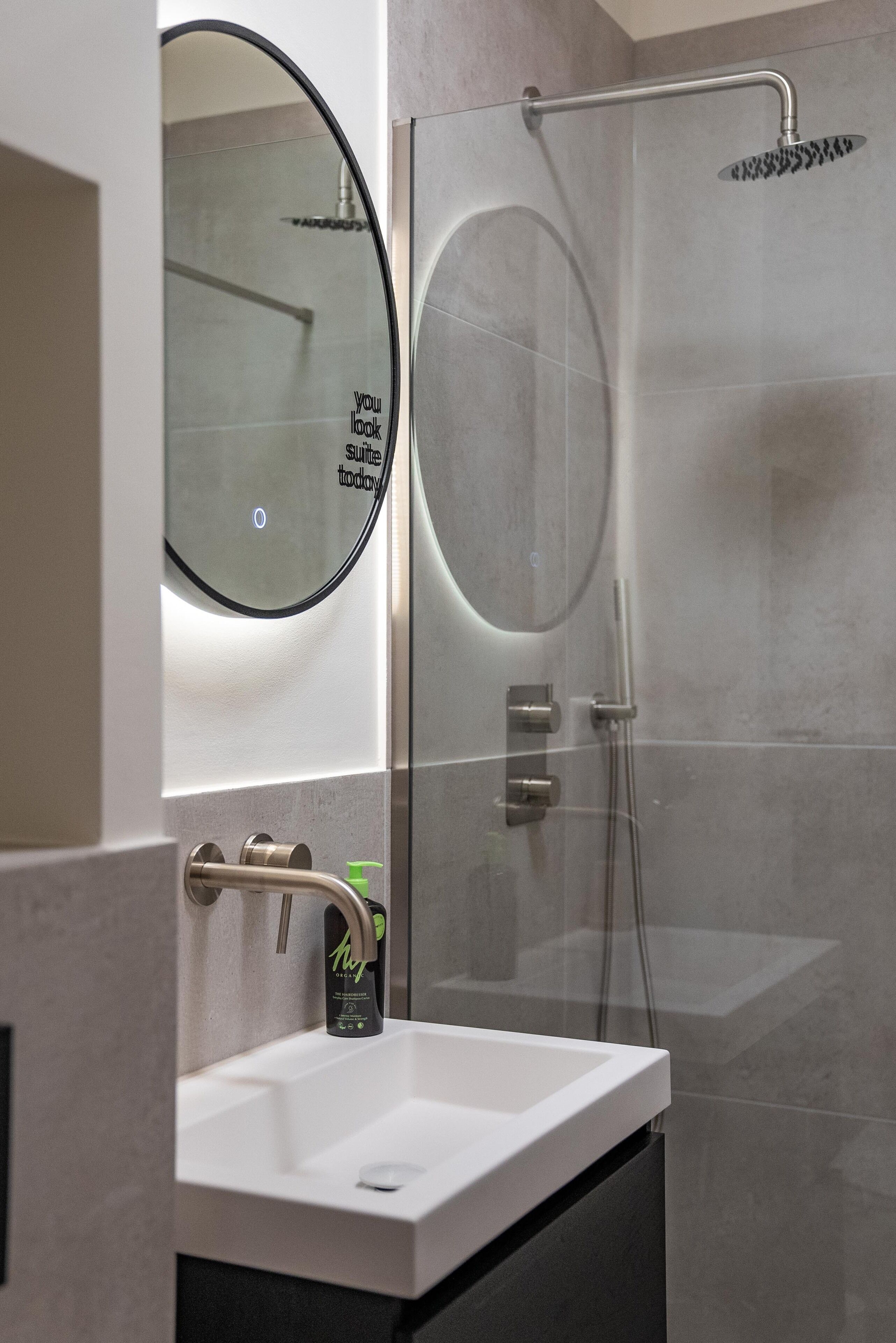 A modern bathroom with a glass-enclosed shower, a white sink, and a round mirror.