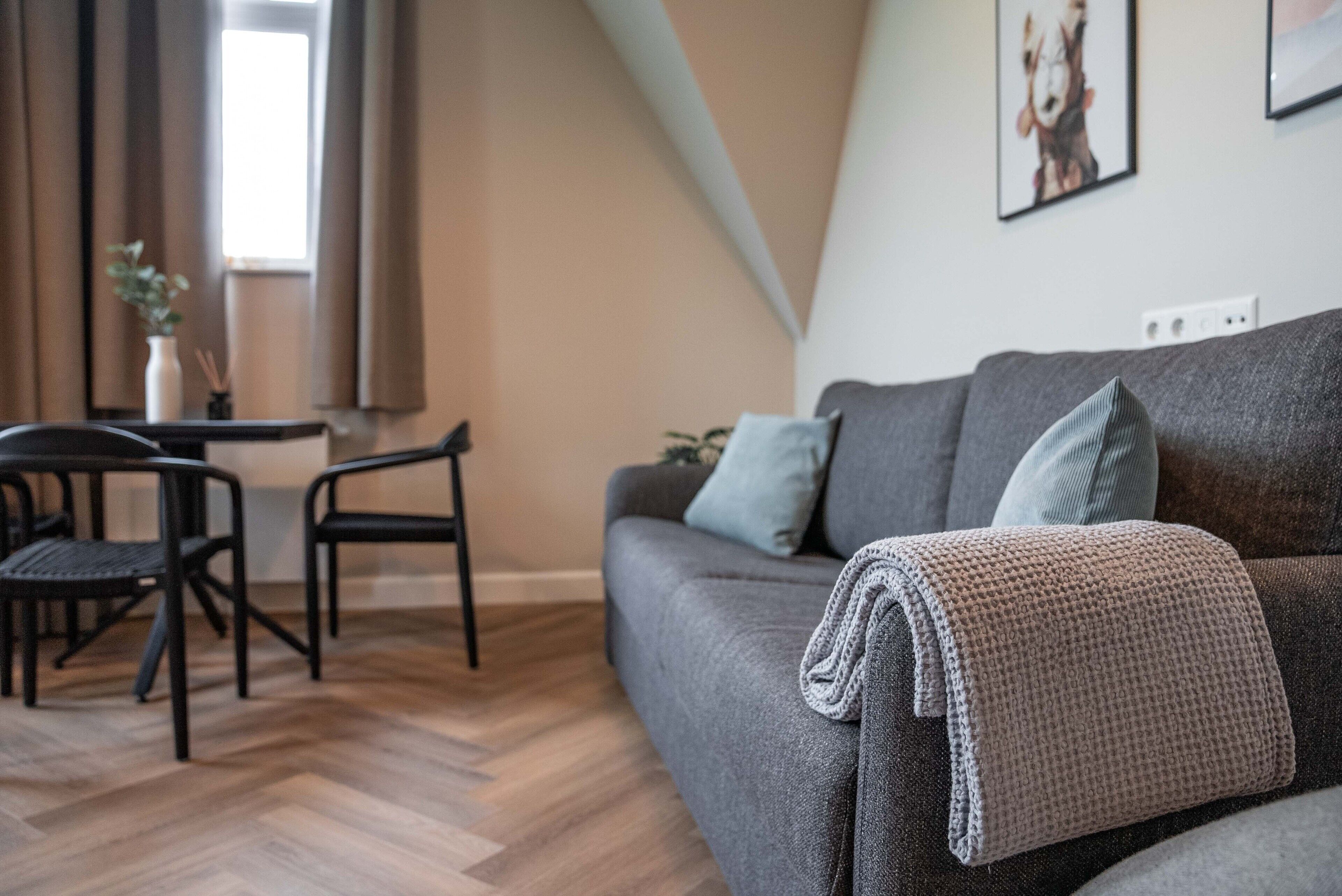 Een moderne woonkamer met een grijze bank, een salontafel en twee zwarte stoelen.