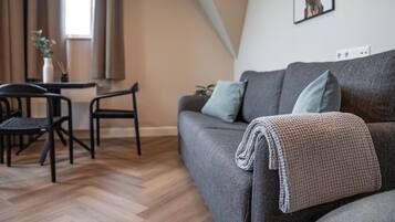 Een moderne woonkamer met een grijze bank, een salontafel en twee zwarte stoelen.