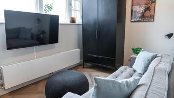 A modern living room with a flat-screen TV, a grey sofa, a black cabinet, and a radiator.