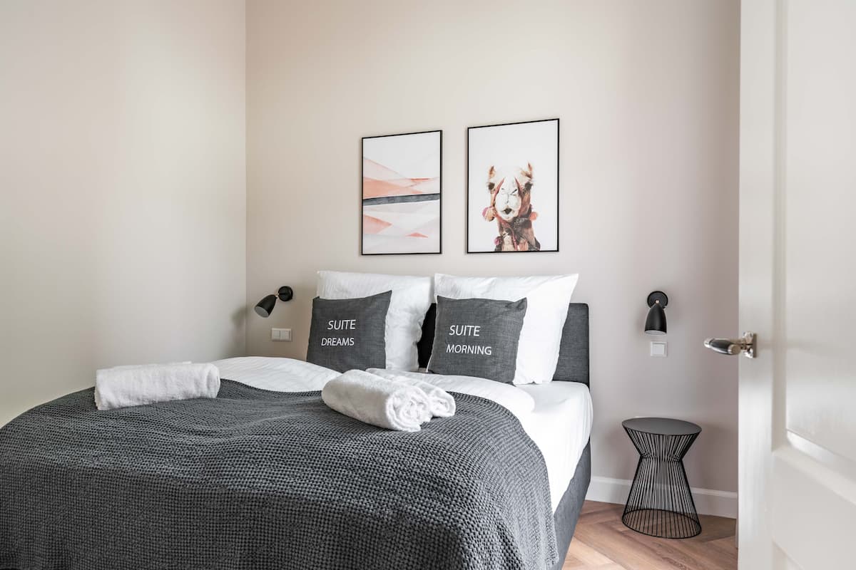 A neatly made bed with a gray bedspread and two pillows labeled "SUITE DREAMS" and "SUITE MORNING".