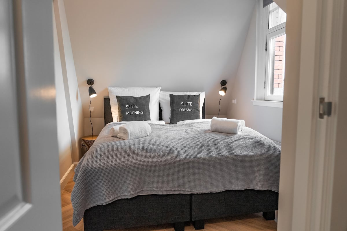 A bedroom with a bed, two bedside lamps, a window, and a door.
