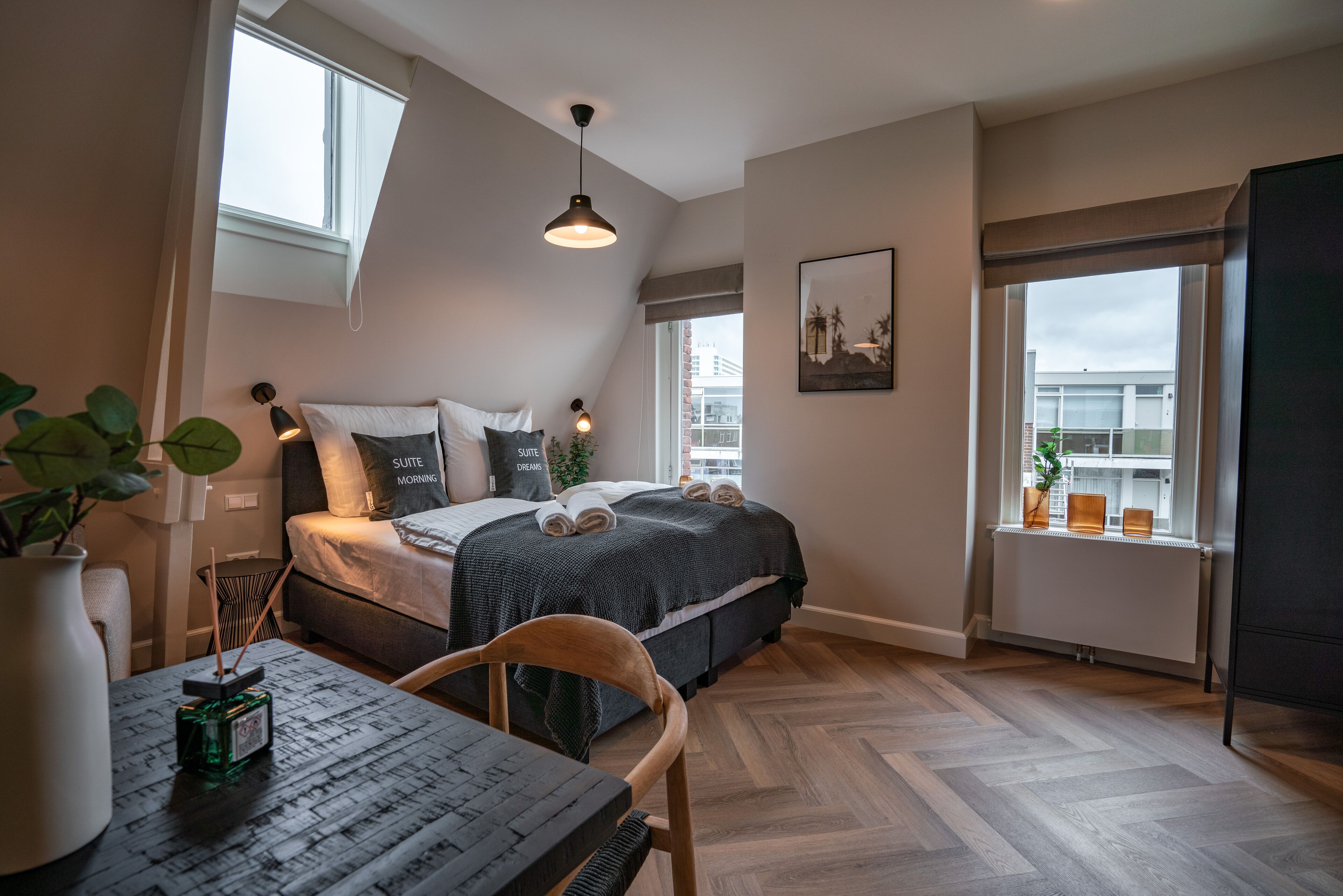 A bedroom with a bed, bedside table, chair, and a window with a view of buildings.