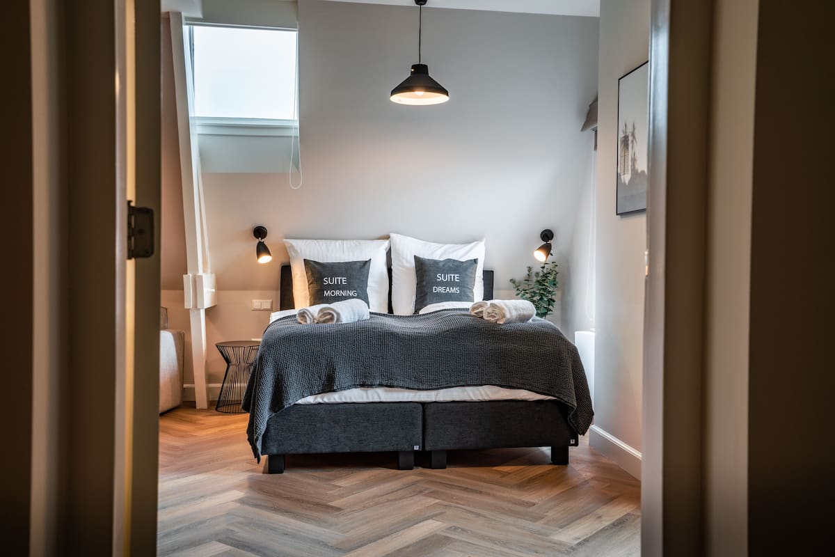 A modern bedroom with a bed, bedside lamps, and a view of the city skyline through a window.