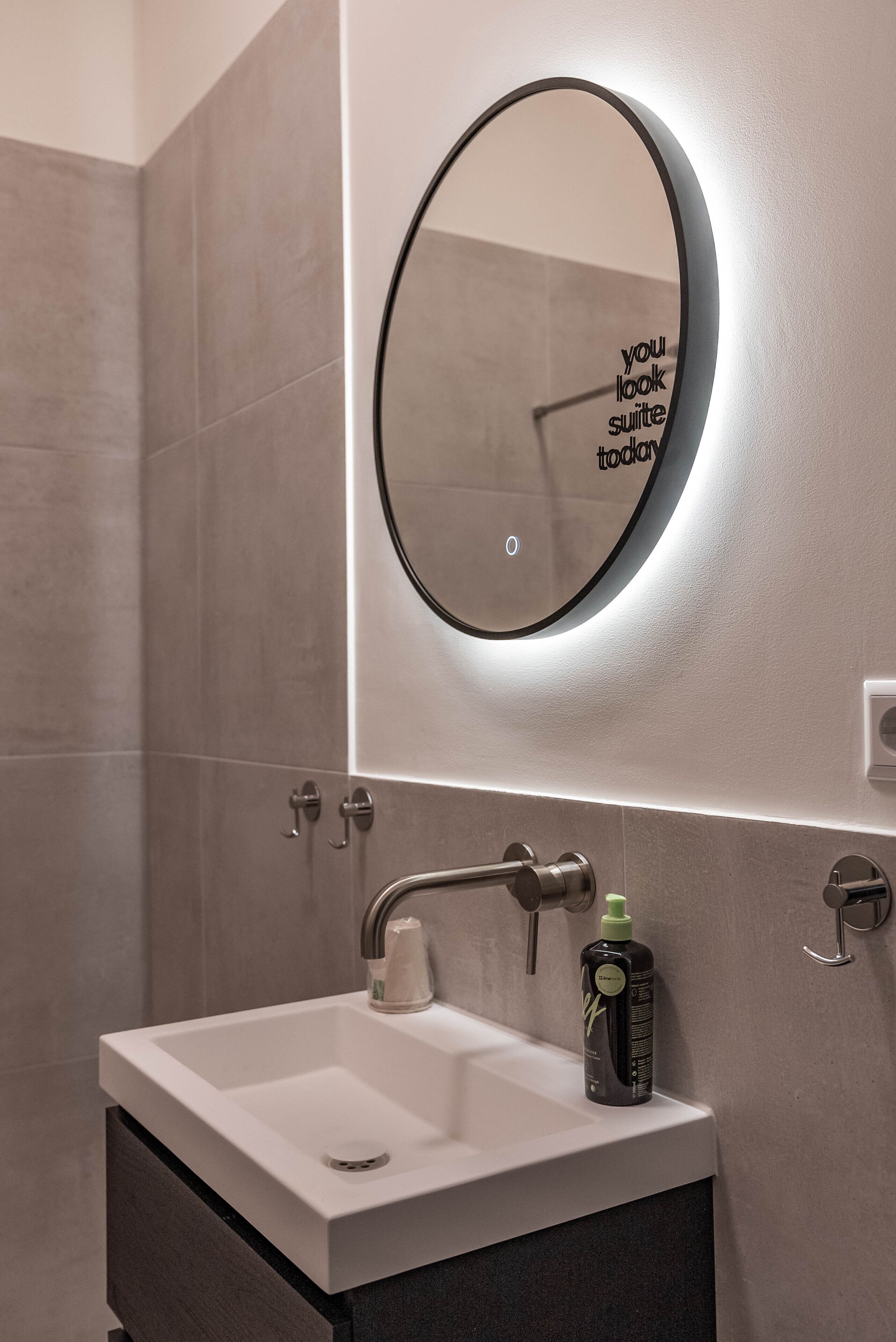 A bathroom with a white sink, a round mirror with a black frame, and a wall-mounted light.