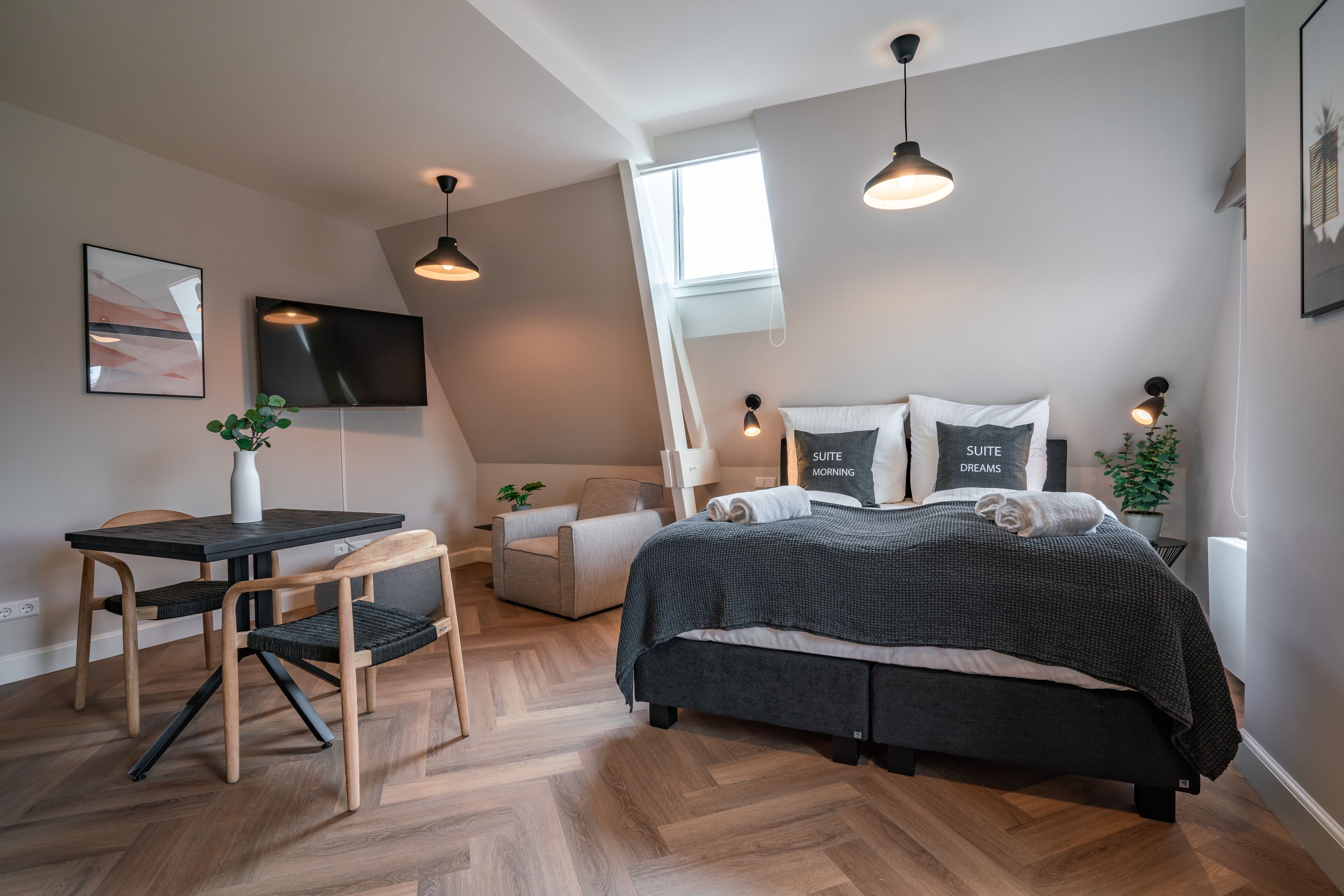Een moderne slaapkamer met een bed, bureau, stoel en een potplant.