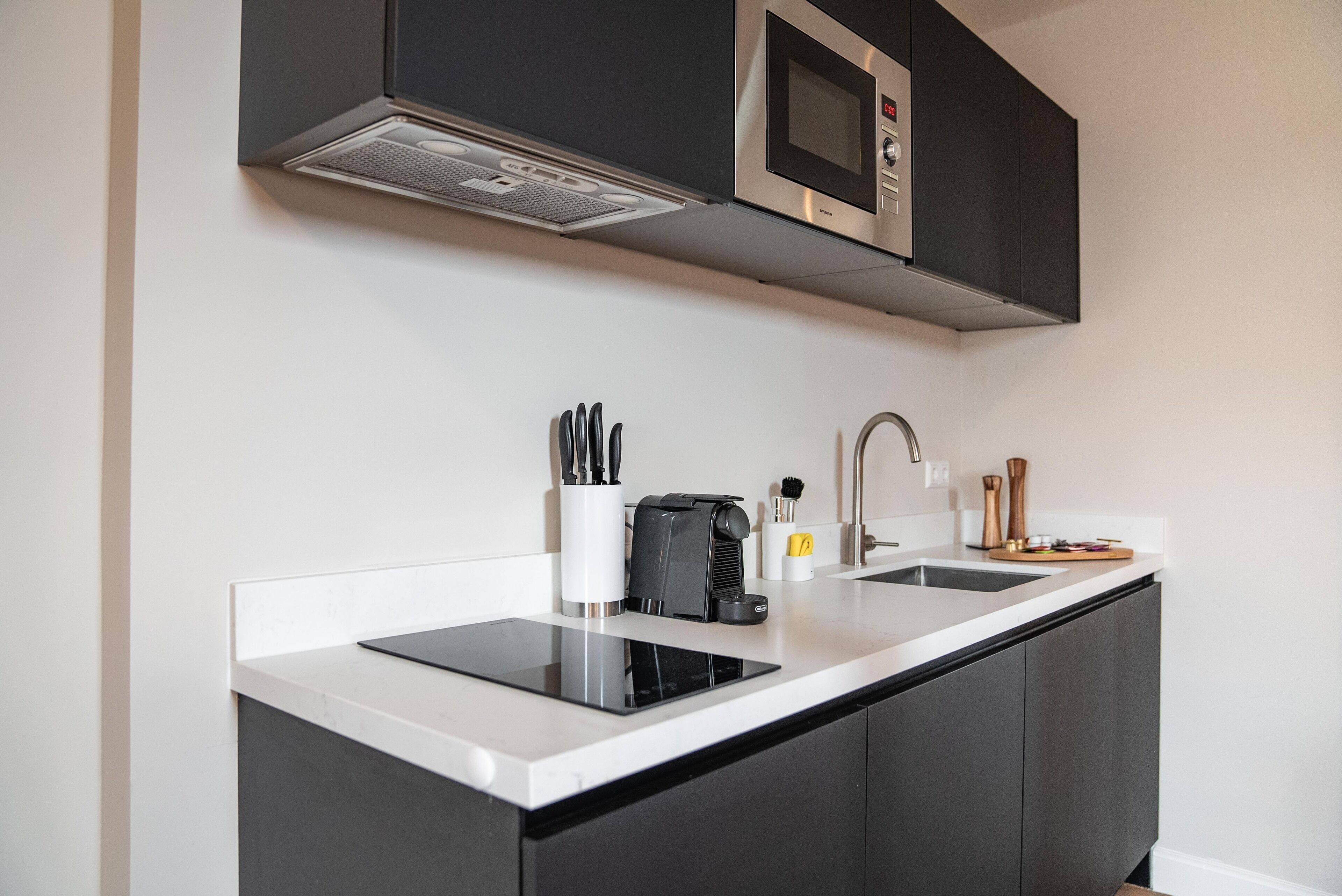 A modern kitchen with black cabinets, a white countertop, a built-in microwave, and a coffee maker.