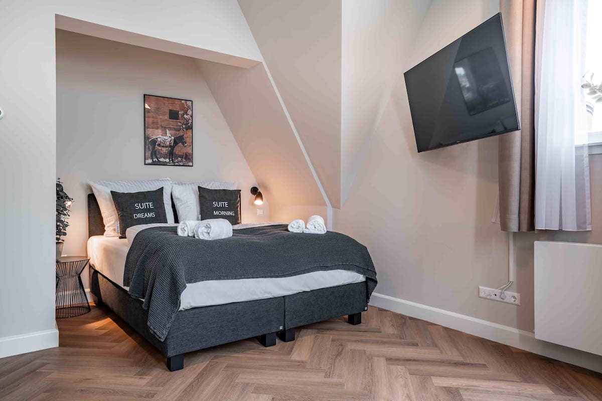 A modern bedroom with a bed, a wall-mounted TV, and a painting.