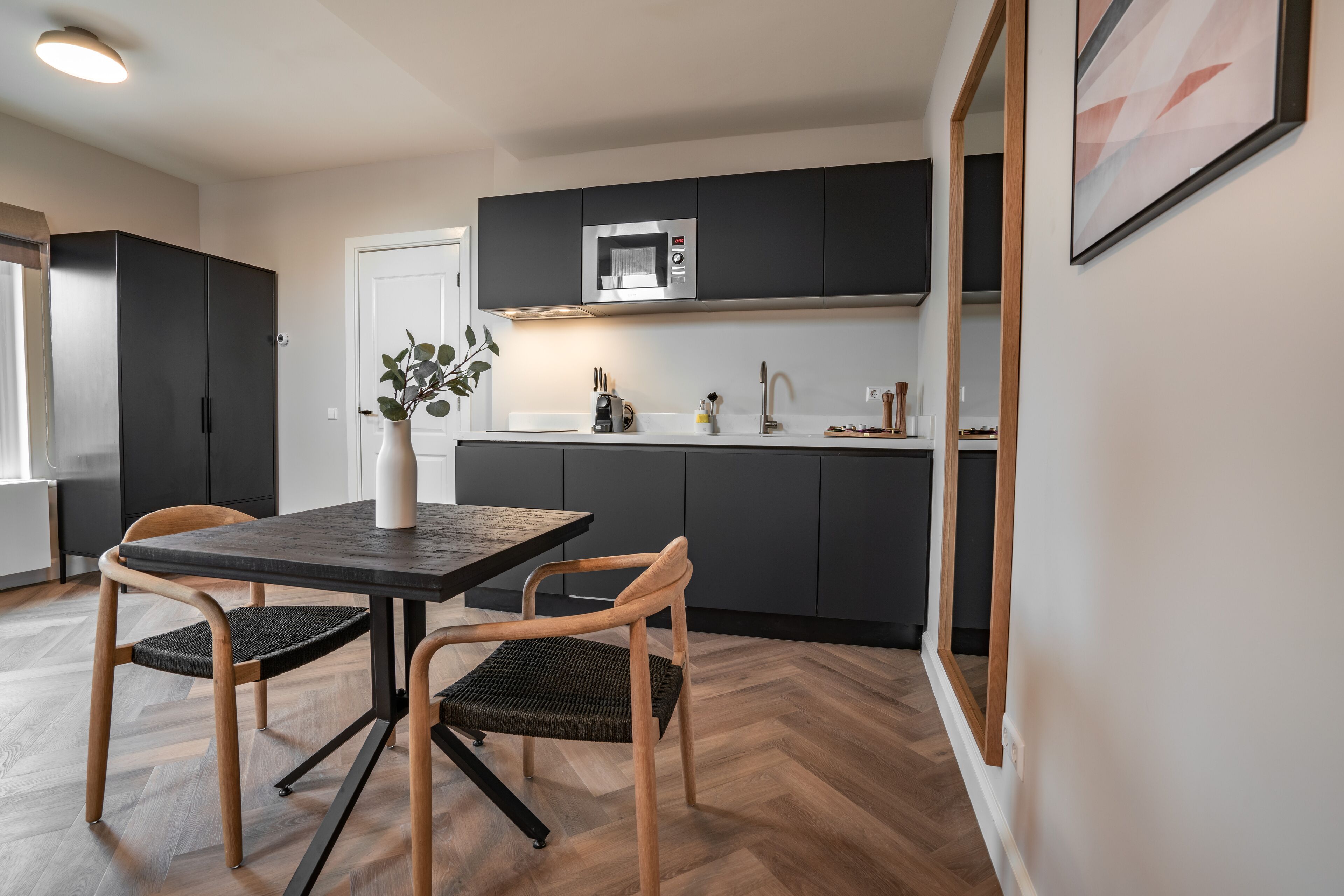 A modern kitchen with dark cabinets, a microwave, and a dining area with a table and chairs.