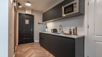 A modern kitchen with dark cabinets, a stainless steel microwave, and a wooden herringbone floor.