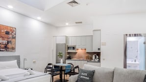 A modern hotel room with a bed, a grey sofa, a dining area with a table and chairs, a kitchen with a fridge and microwave, and a bathroom with a glass door. - Limehome Madrid Calle de Don Ramón de la Cruz (Madrid)
