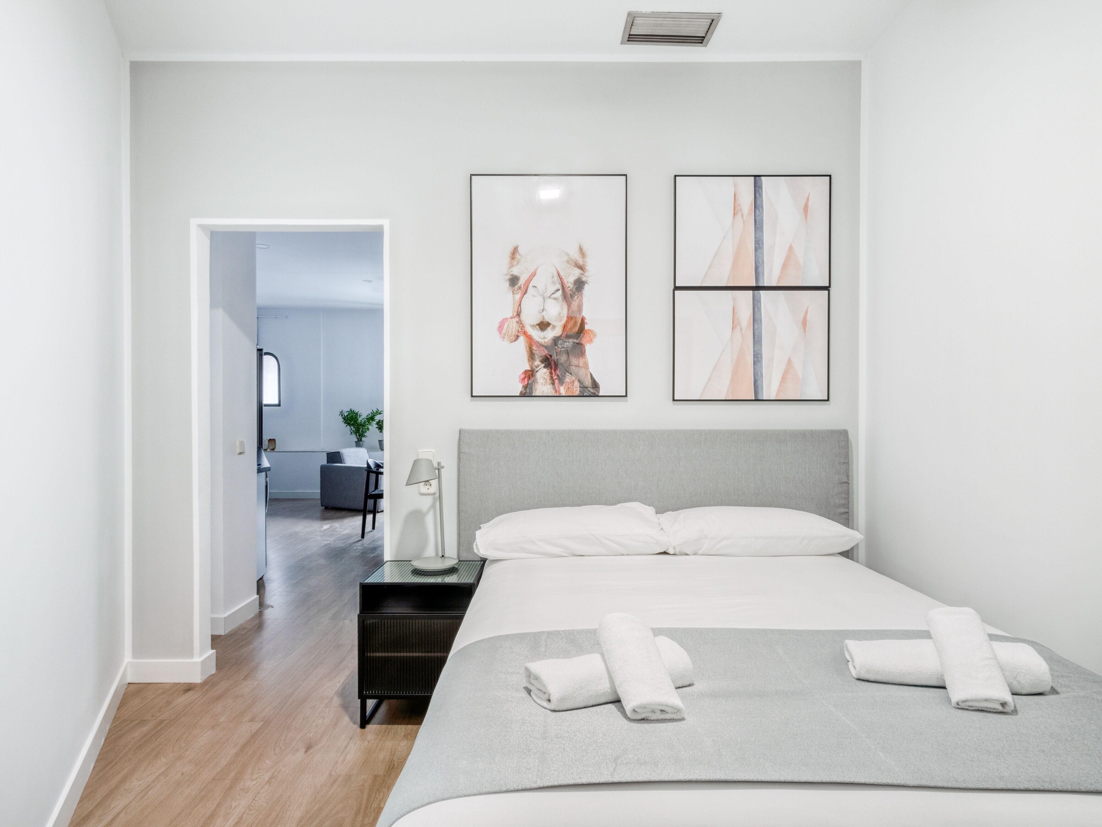 A modern hotel room with a large bed, a bedside table with a lamp, and artwork on the wall.