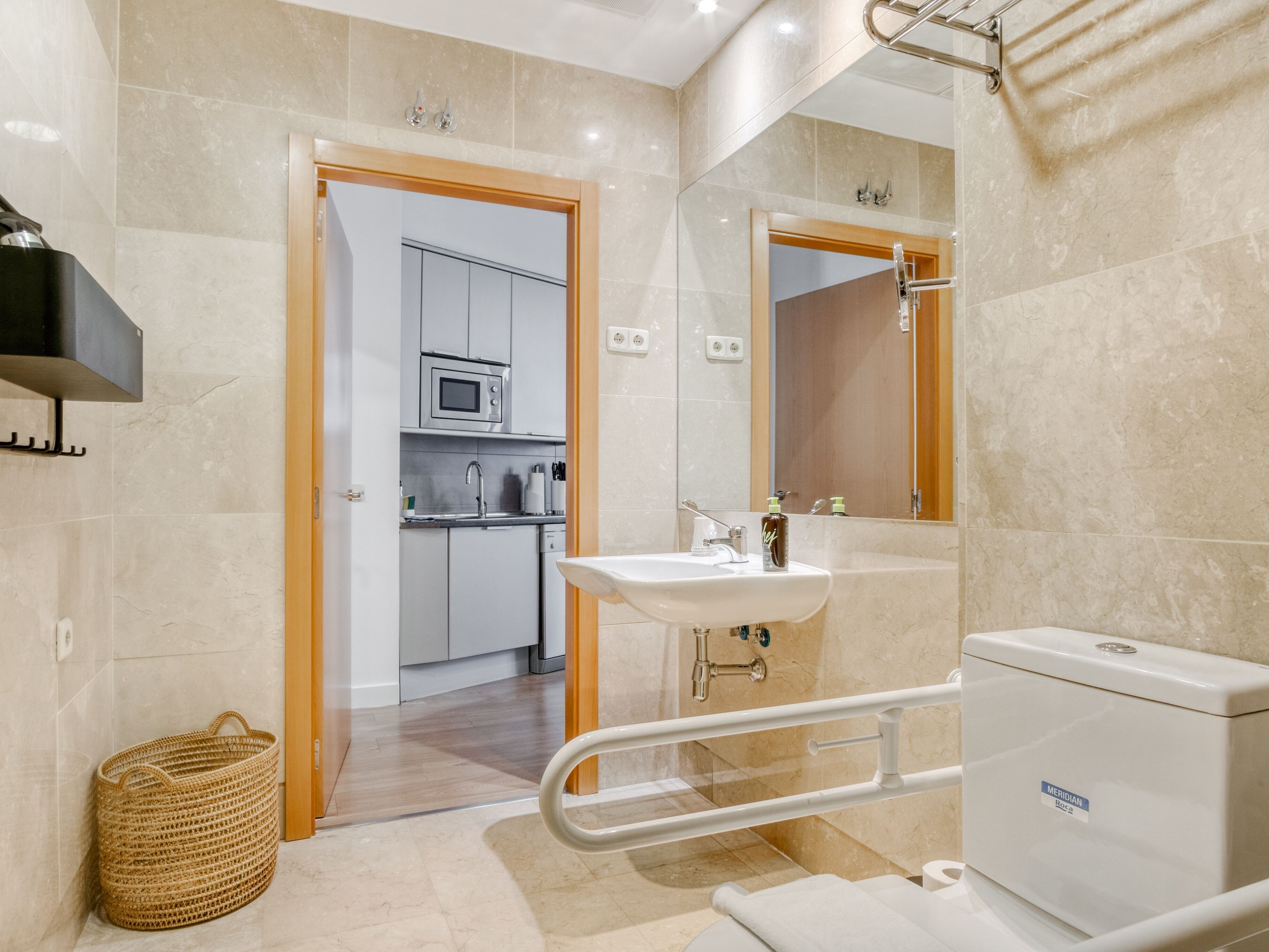 Une salle de bain moderne équipée d’un lavabo, de toilettes et d’une douche. Elle comprend une porte en bois donnant sur une cuisine avec un four à micro-ondes et des placards.