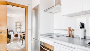 A modern kitchen with white cabinetry, stainless steel appliances, and a wooden door leading to a dining area. - Limehome Madrid Calle de Don Ramón de la Cruz (Madrid)