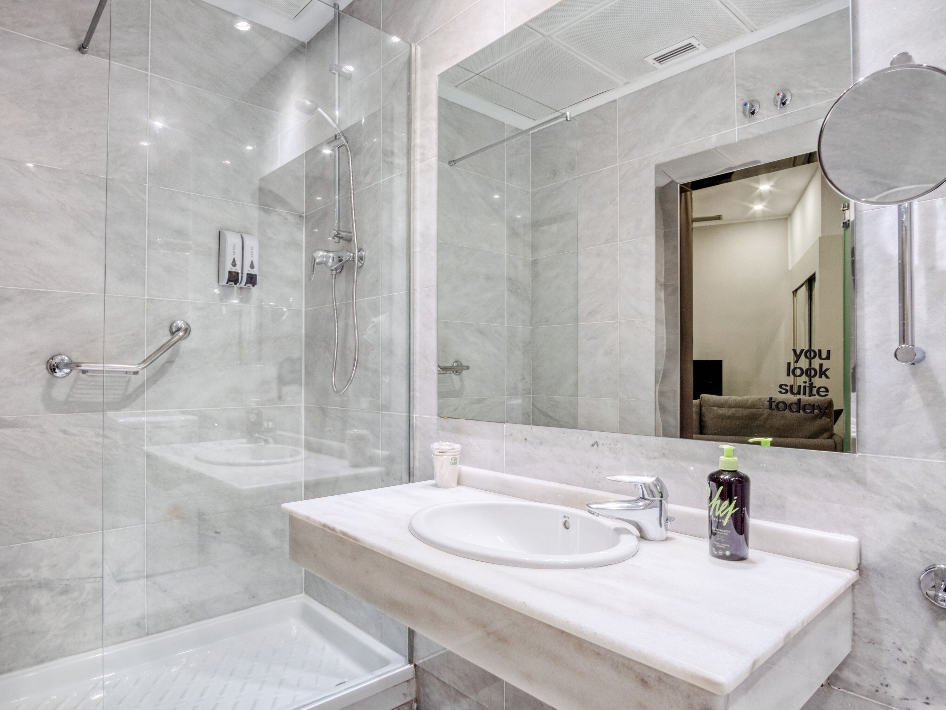 A modern bathroom with a glass shower enclosure, a white sink with a mirror, and a towel rack.