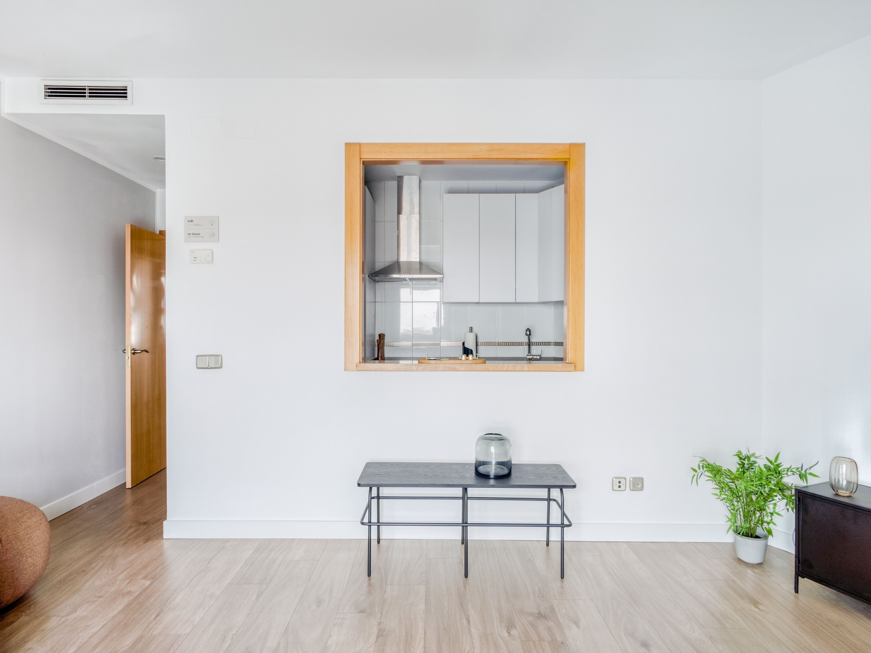 A modern kitchen with a wooden-framed window, a small table with a glass container, and a potted plant.