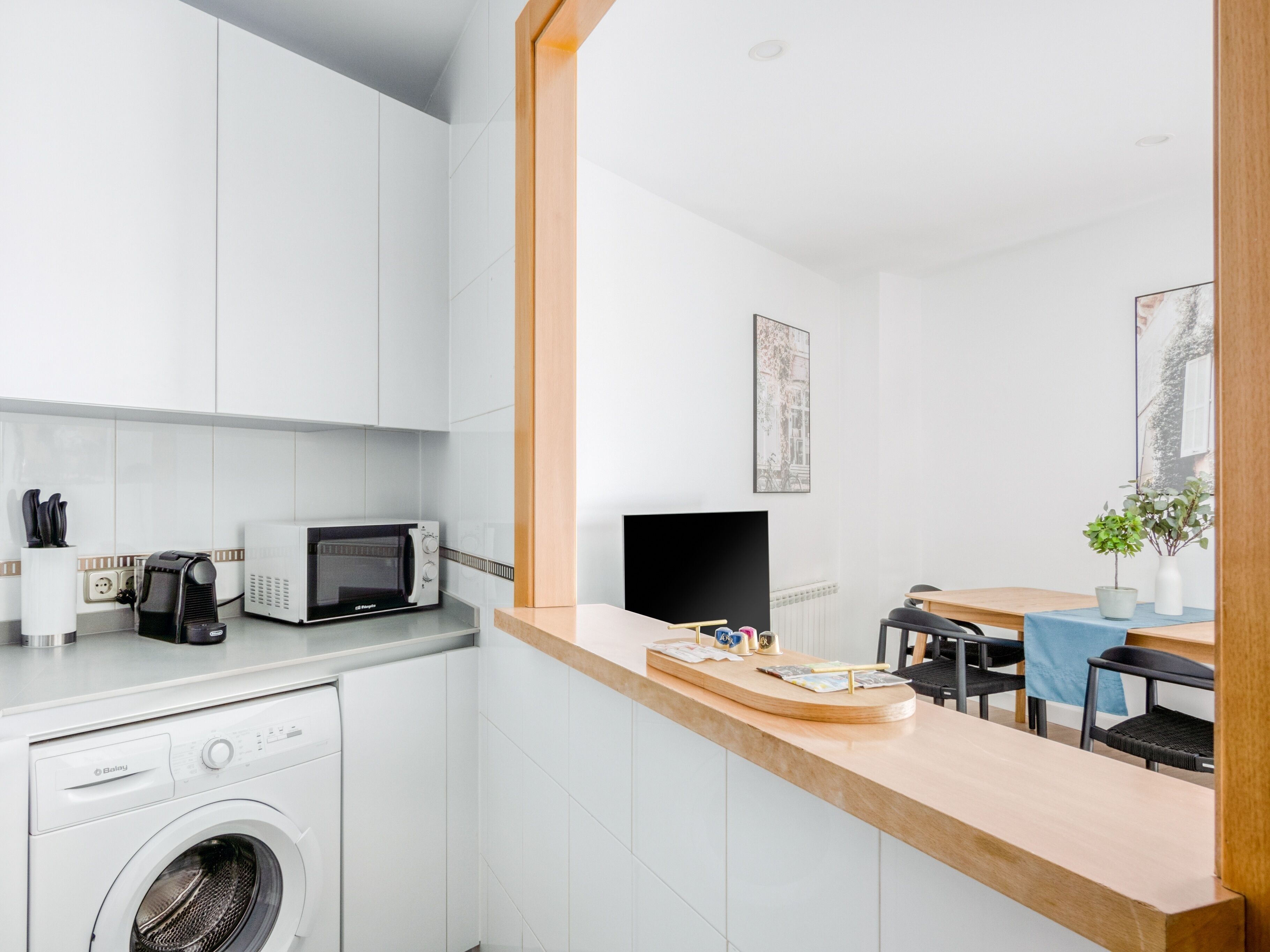 A modern kitchen with a washing machine, a microwave, and a dining area with a table and chairs.