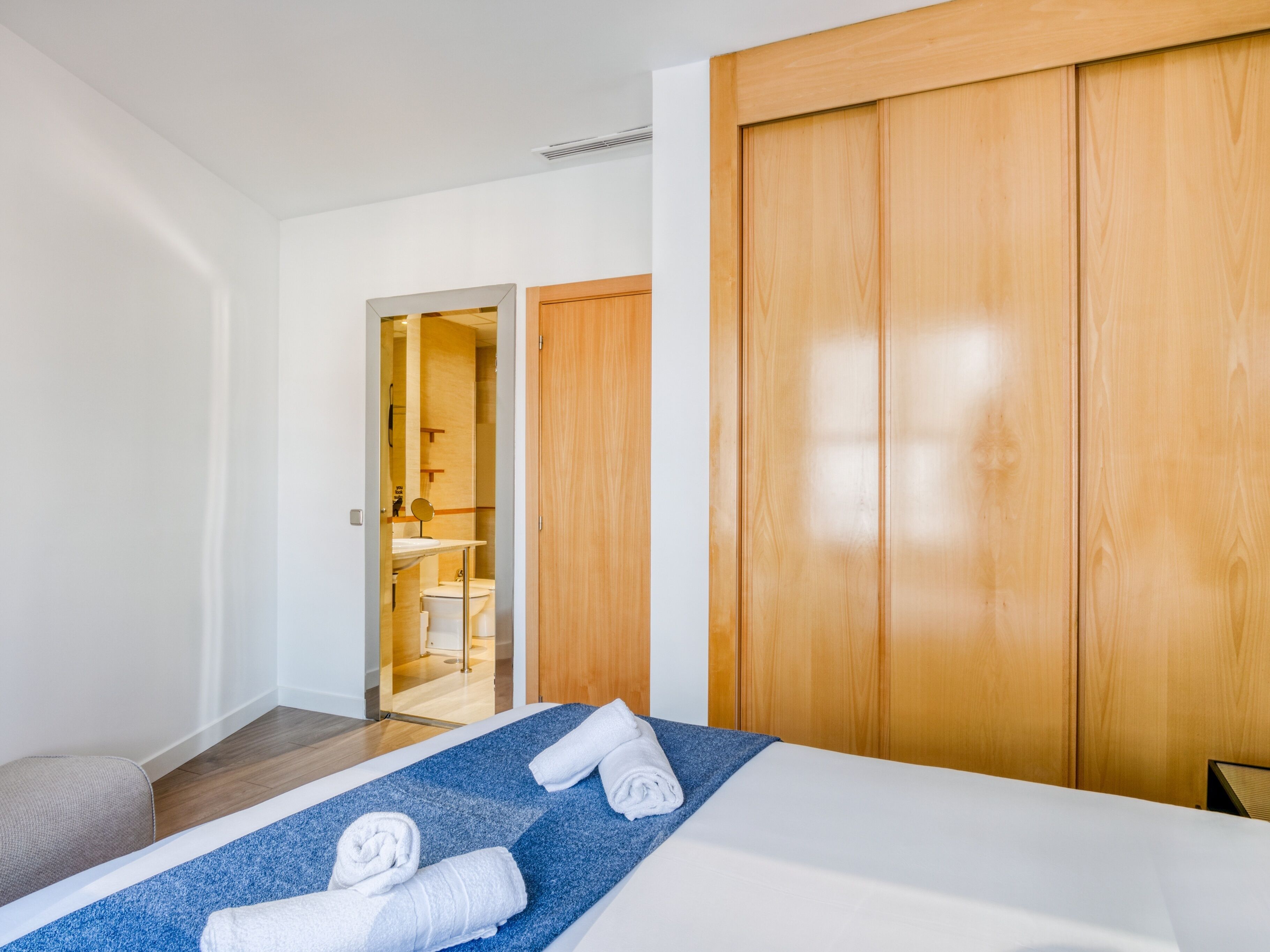 A hotel room with a bed, a wooden wardrobe, and a bathroom visible through an open door.