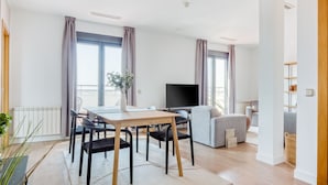 A modern living room with a dining table, chairs, a sofa, a TV, and large windows with curtains. - Limehome Madrid Calle de Don Ramón de la Cruz (Madrid)