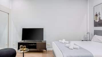 A modern hotel room with a flat-screen TV, a bed with neatly folded towels, a small side table with decorative vases, and a minimalist nightstand.