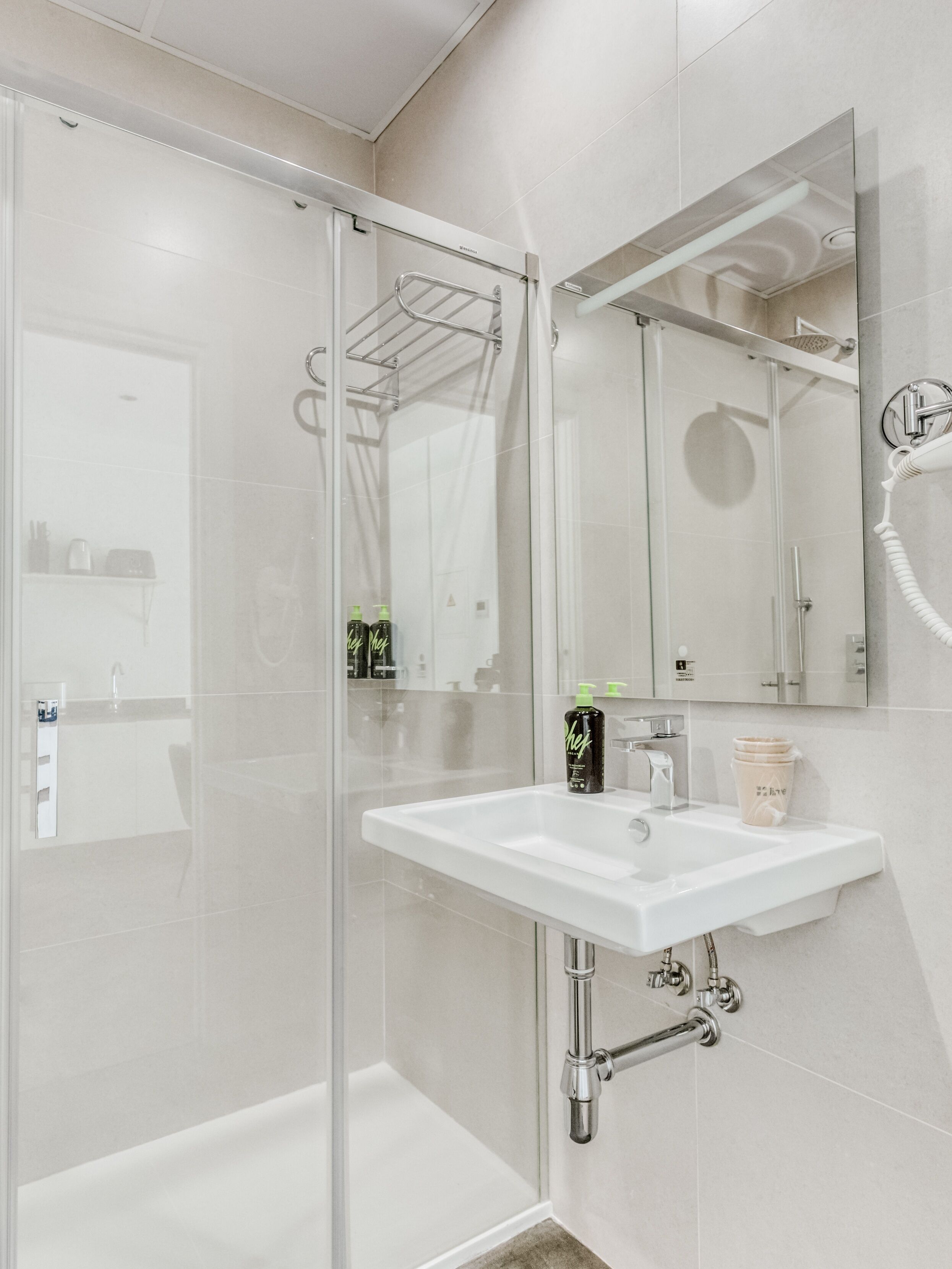 Un baño moderno con cabina de ducha de vidrio, un lavabo blanco y un espejo grande.
