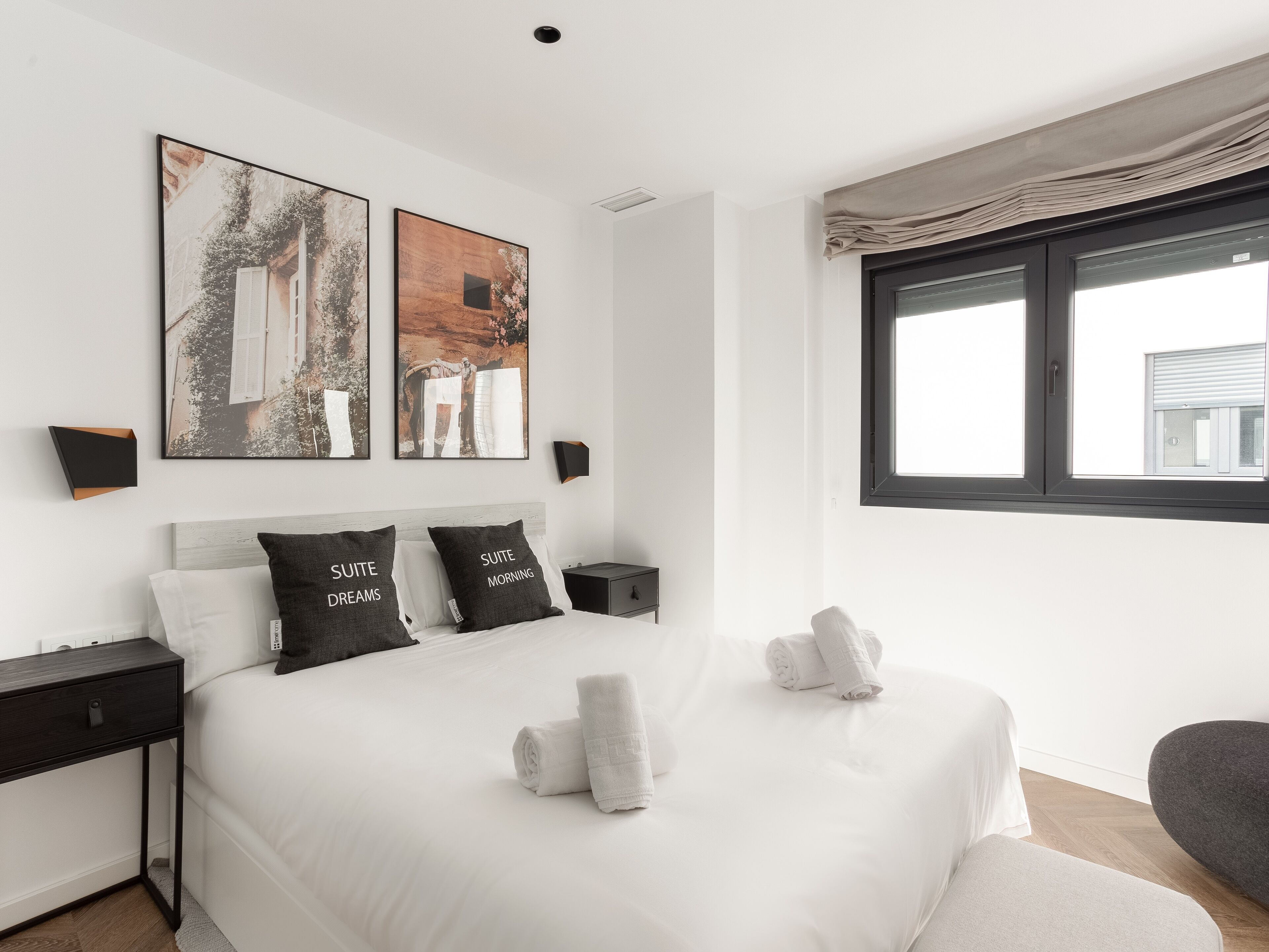 A modern bedroom with a large bed, two bedside tables, a nightstand, and a window with curtains.
