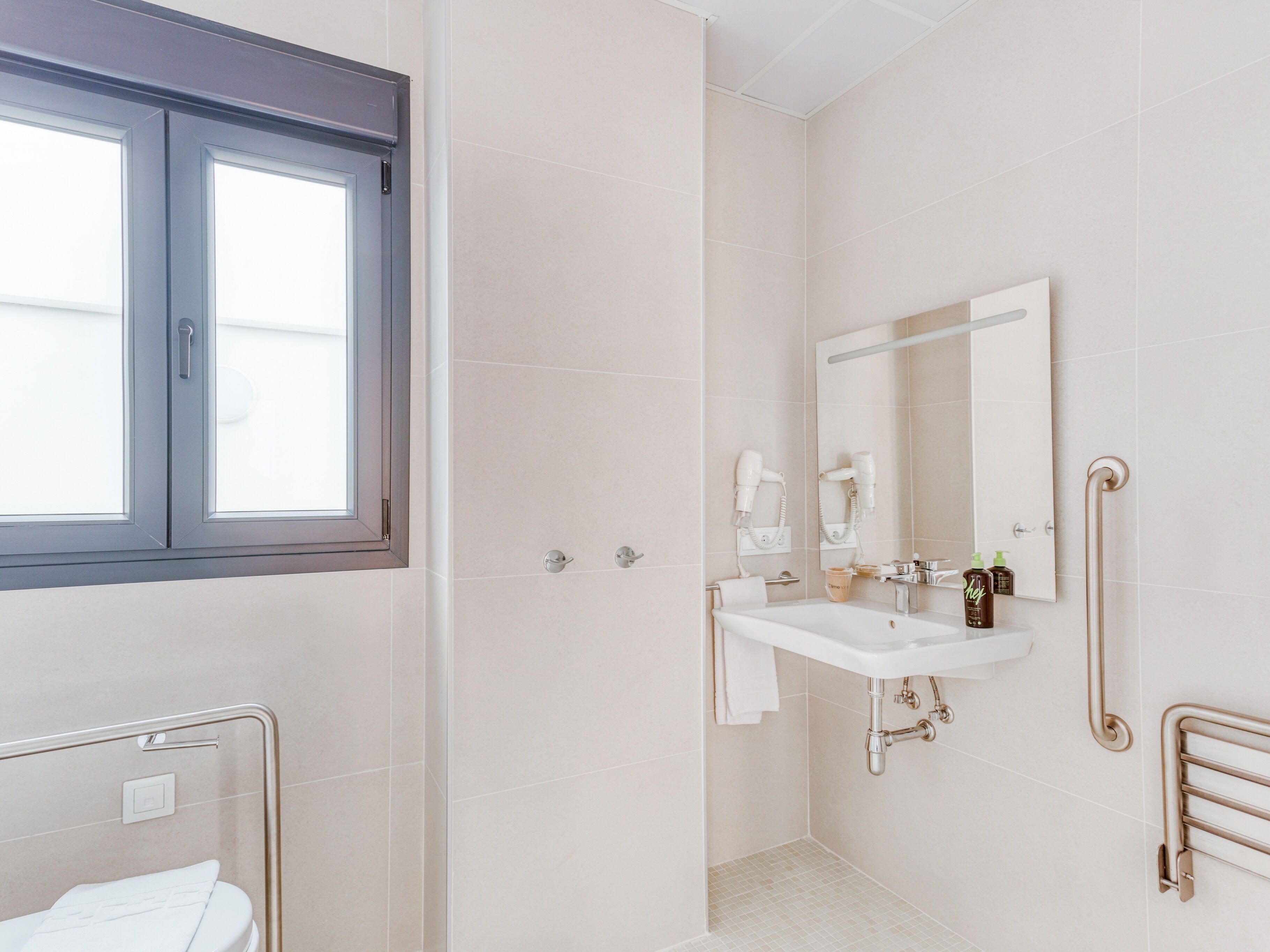 Un baño moderno con un ventanal grande, un lavamanos blanco, un espejo y una zona de ducha.